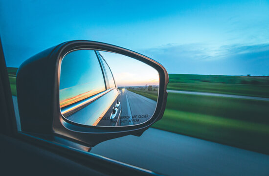 An image of a car's sideview mirror showing the roadd behind and what appears to be a sunset.